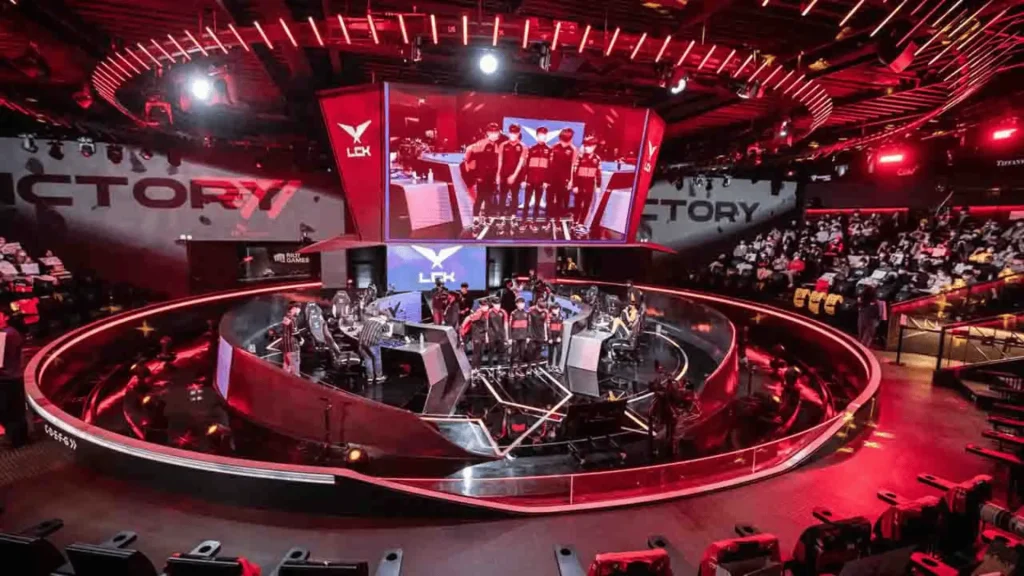LCK esports arena stage with teams competing, red lighting, large screens, crowd seating, and professional League of Legends match setup