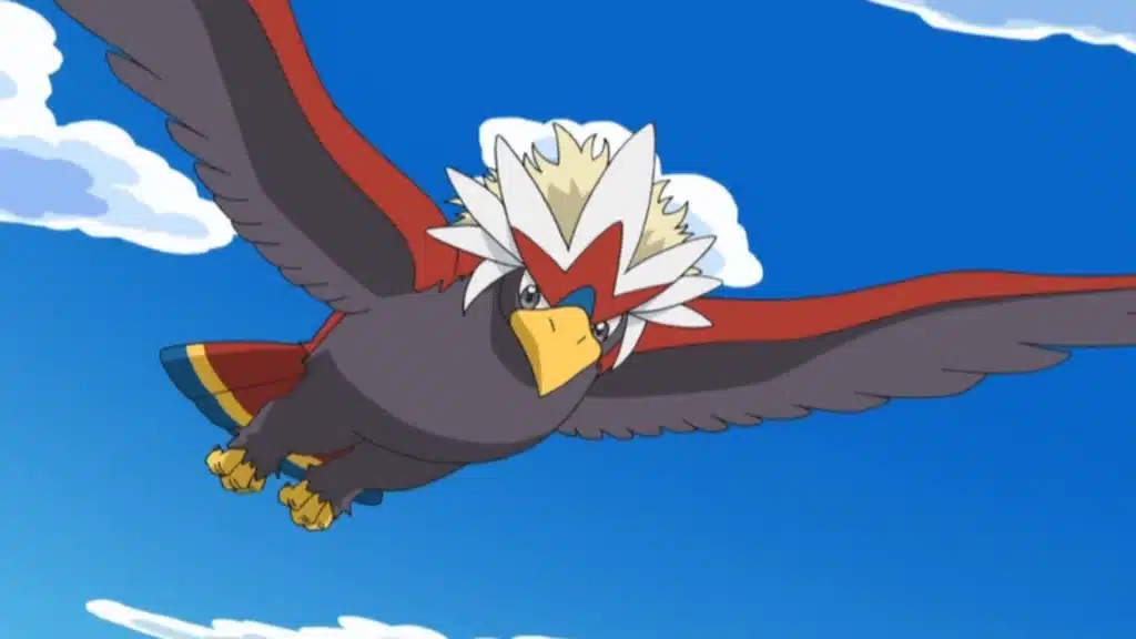 Braviary flying with wings spread wide, showing its bold red white crest and strong body against a blue sky