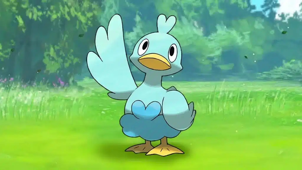 Ducklett standing on grass with one wing raised, showing its light blue body and small beak in a bright outdoor setting