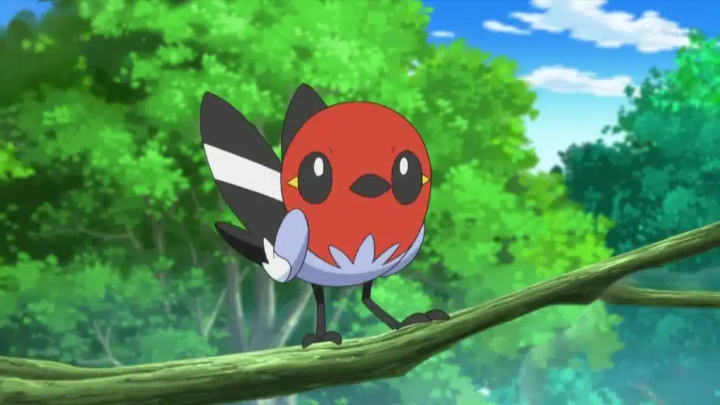 Fletchling perched on a branch with a red face and black wings, set against a bright green forest background