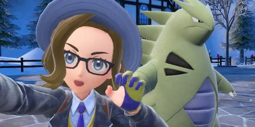 Trainer taking selfie with Tyranitar in snowy town setting, wearing hat, glasses, and school uniform